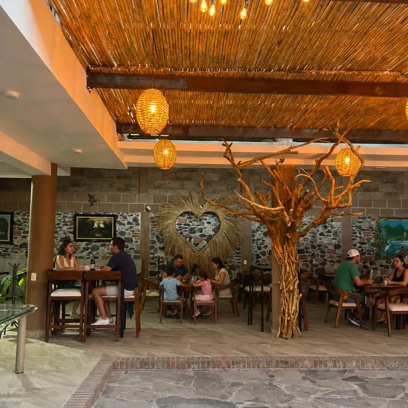 Terraza con techo de carrizo y árbol decorativo en Mariscos Muelle 27, Jardines del Cimatario